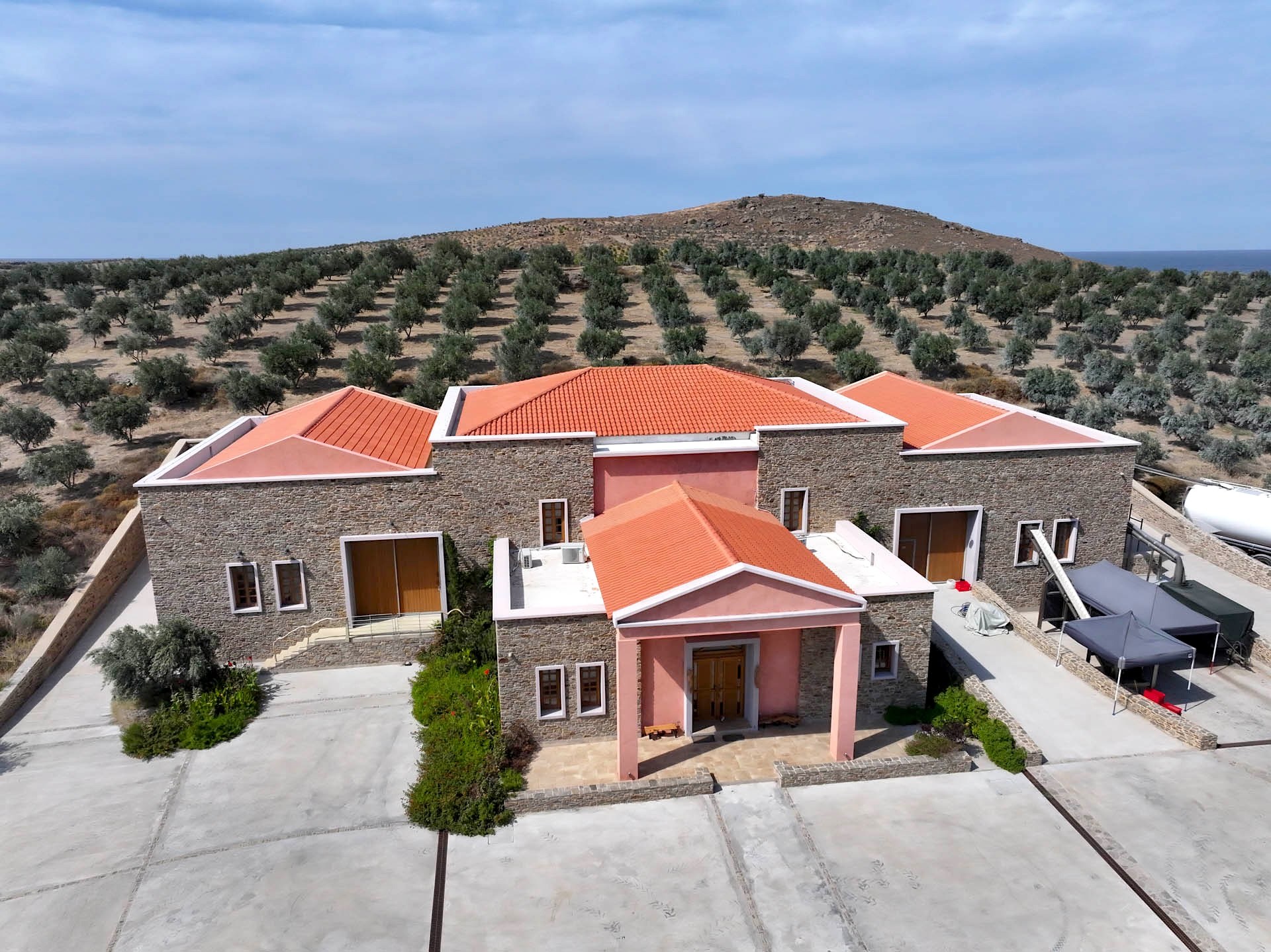 The mill from the air: stone walls, tiled roofs and the pink portico, groves all around