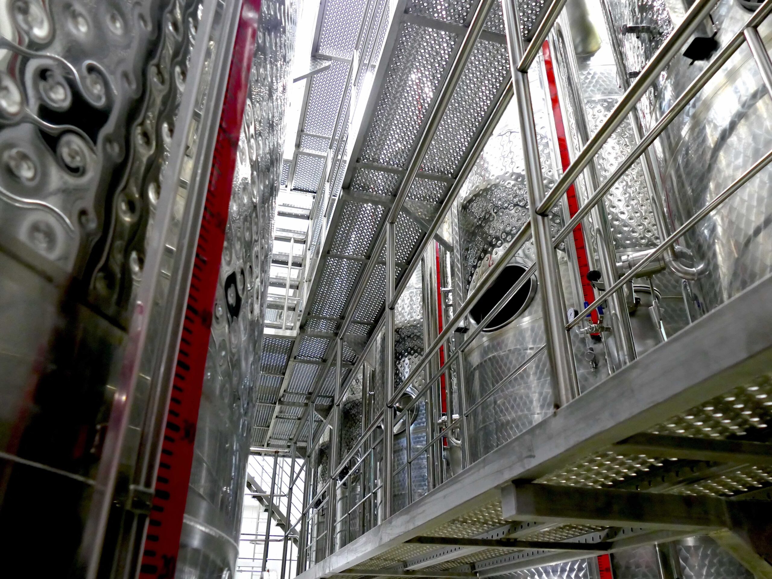 Stainless-steel storage tanks rising beside the walkway, their level gauges in red