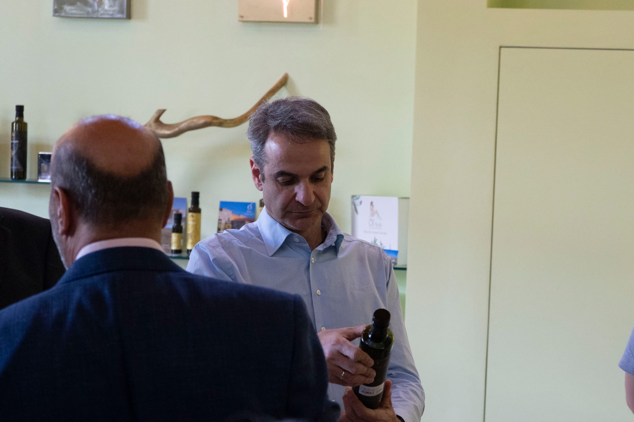 Prime Minister Mitsotakis examines a bottle of extra virgin olive oil beside shelves of Ol-eve products